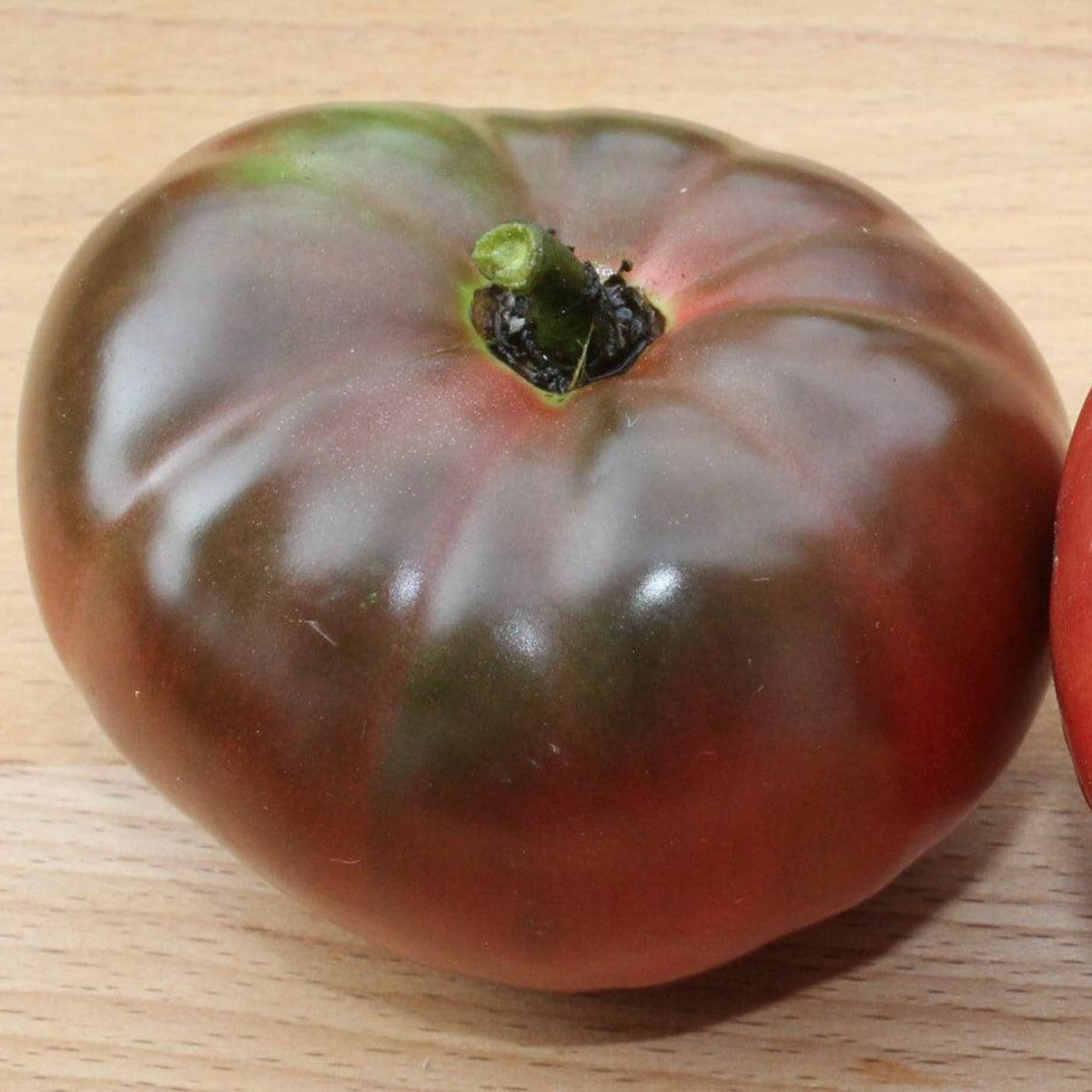 Ripe Black Krim heirloom tomato with dark purple-red skin, green shoulders, and a large, slightly flattened beefsteak shape, known for its rich, flavorful taste.