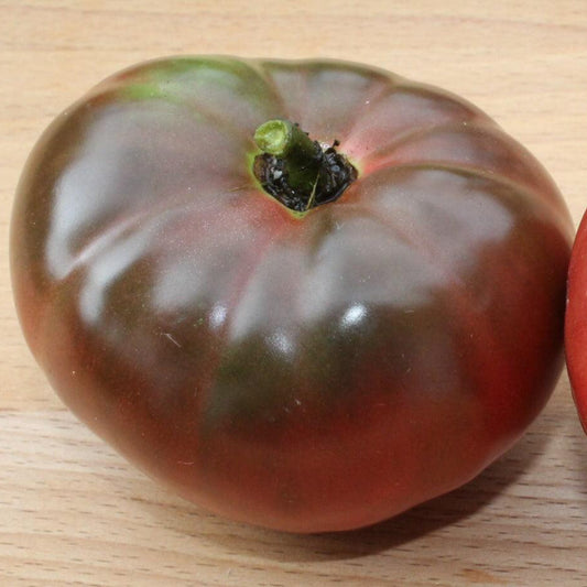 Ripe Black Krim heirloom tomato with dark purple-red skin, green shoulders, and a large, slightly flattened beefsteak shape, known for its rich, flavorful taste.