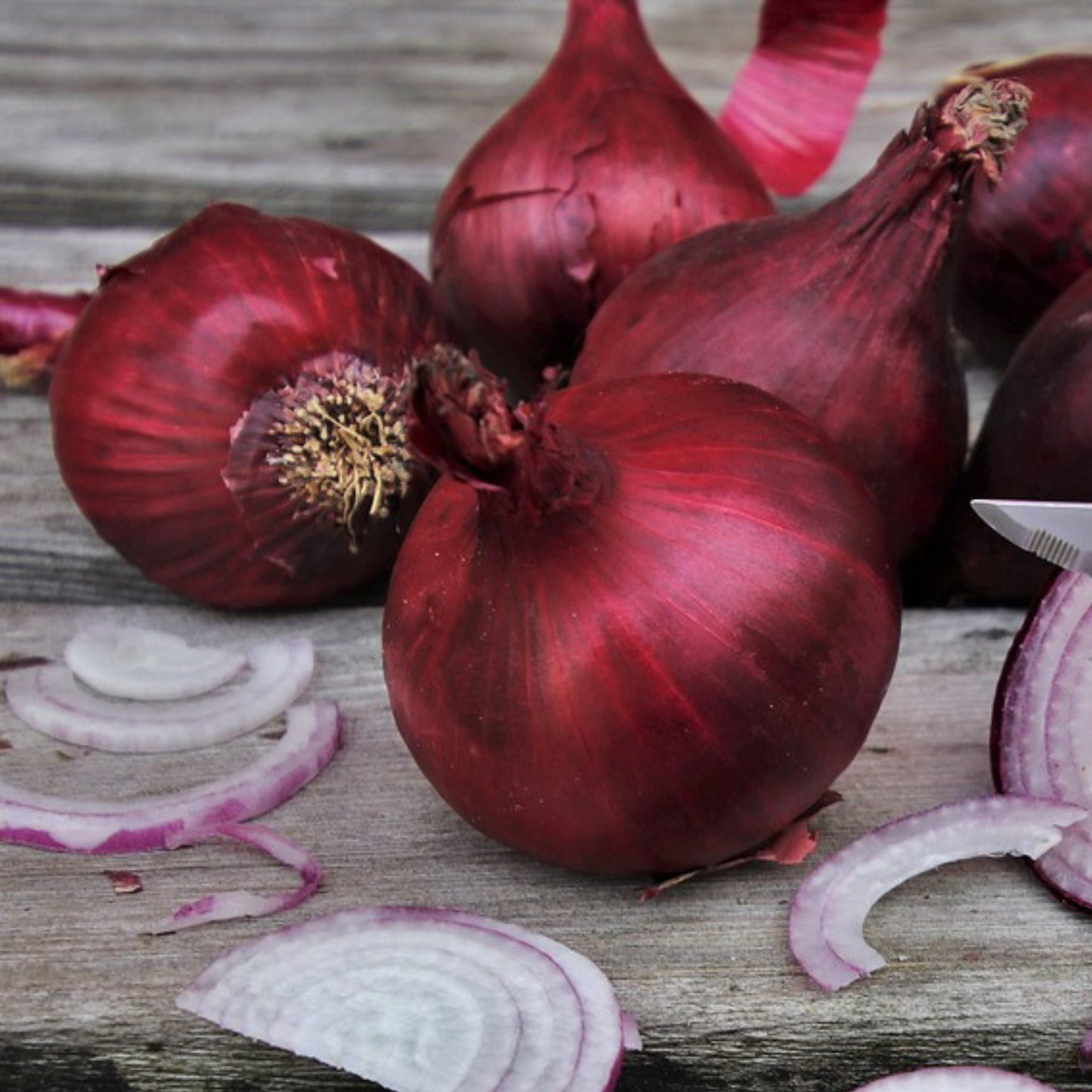 Red onions with some sliced on a wooden surface